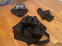 Three pairs of binoculars arranged on a hardwood floor, each paired with a carrying bag or case