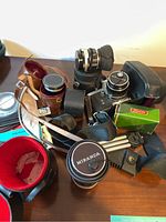 Photo showing the Miranda camera body, several lenses with caps, leather cases, and a green Sixon box on a wooden surface.