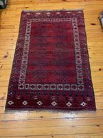 Full top-down image of a red area kilim rug with geometric designs and decorative border on a hardwood floor.