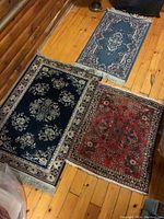 Three small carpets placed on wooden floor showing size and pattern variations.