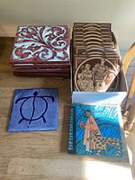 Full view of assorted ceramic tiles including Italian 8x8 inch tiles with red-blue white leaf patterns, Mintons 6x6 inch historic figure tiles, a blue turtle tile, and a colorful person and cheetah tile.