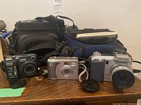 Nikon Coolpix 880, HP Photosmart 935, Minolta Dimage 7 cameras with storage and carrying cases, displayed on a wooden surface.