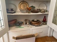 Wide shot of lower and upper shelves containing multiple bowls, serving trays, decorative glass and ceramic kitchenware items.