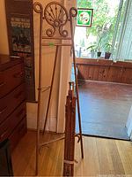 Full view of two vintage easels, including a bamboo easel with decorative curls and a folded wooden easel leaning against the wall near a window.