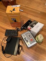 Image of all electronic items and accessories on wood floor, including Kodak EasyShare printing dock, router, remote control, tripods, boxed headphones, and accessories.