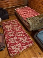 Two-piece red and white floral patterned futon mattress on wooden floor next to bed