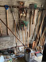 View showing assortment of garden rakes, shovels, brooms and hand tools stored against brick wall.