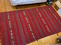 Angled view showing red kilim rug folded under bed, illustrating texture and pattern.