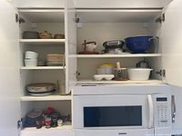 Open kitchen cabinet showing various ceramic pots, ramekins, colander, and small kitchenware items