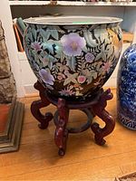 Full view of the ceramic fishbowl planter on the wooden stand showing floral exterior design and stand structure.