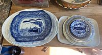 Overall view showing stacked ceramic and porcelain serving dishes with blue and white designs, along with metal dishes with blue decoration and inscription.
