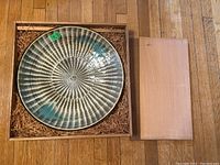 Top view of the ceramic plate showing the radial texture and multicolor glaze inside a wooden box.