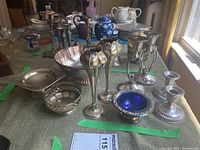 Front view of assorted silver plated items including candlesticks, bowls, and trays arranged on a table.