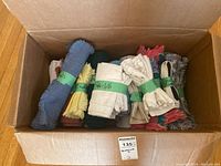 Open cardboard box with assorted rolled and bundled table linens including napkins, placemats, and tablecloths in multiple colors.