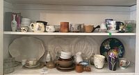 Shelf with assorted kitchenware including plates, teacups, creamers, ramekins, and wooden bowls.