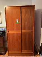 Photo showing full view of teak wardrobe with two sliding doors and recessed square handles on each door.