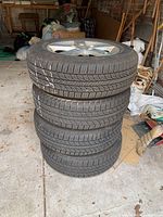 Stack of four tires mounted on 5-spoke Mazda alloy wheels
