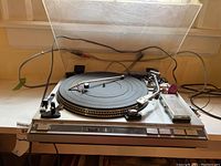 Full view of the JVC L-F66 turntable with dust cover raised, showing tonearm, platter, control buttons, and accessories nearby.