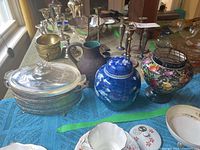 Wide view of the lot showing four pieces on a blue cloth including the silver plated stand with serving dish and three ceramic vases