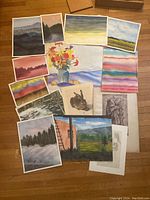 Photo showing a variety of assorted unframed watercolour paintings and sketches arranged on the floor, including landscapes, floral still life, wildlife sketch, and abstract washes.