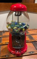 Front view of red metal and glass gumball machine filled with assorted glass marbles
