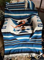 Full view of the woven serape blanket draped over a chair showing the striped pattern and central eagle and snake motif.