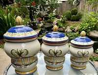 Front view of three covered Pfaltzgraff Villa Della Luna jars in descending size order with clear view of decorative painted pattern and script lettering on each jar.