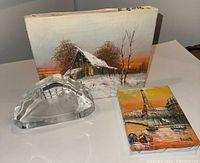 Three items on white surface: crystal baby seal paperweight, 8x10 barn winter landscape painting by H. Fredricks, 5x7 Paris cityscape painting signed Burnett.