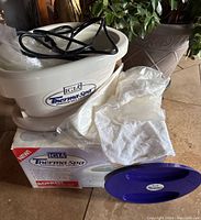 White Therma Spa paraffin wax therapy device with power cord, cotton gloves, plastic bags, and box on floor.