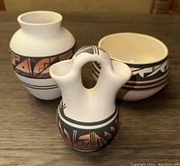Photo of three Navajo pottery vessels on a wooden surface showing varied shapes and traditional painted designs