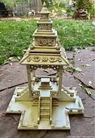 Front view of vintage wooden home worship temple shrine showing central staircase and multi-tiered ornate roof with carved floral and scroll details.