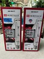 Photo of two boxed 600 watt Hortilux Ceramic HPS grow lamps in red spectrum, showing front of boxes with branding and product details.