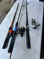 Photo showing three fishing rods with attached reels laid out on surface, displaying overall condition and setup