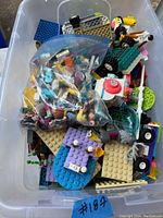 Overhead view of the bin showing loose LEGO Friends bricks in various pastel colors along with some mini-figures in a plastic bag inside the bin.