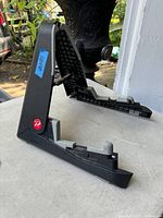 Folding guitar/instrument stand unfolded showing black plastic with gray rubber pads and red circular logo.