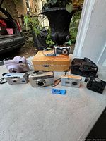 Photo of all eight cameras arranged with Canon PowerShot A460 box showing the variety in the lot.