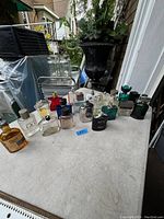 Wide shot of multiple men's cologne bottles grouped on a white table outdoors, in various shapes and conditions