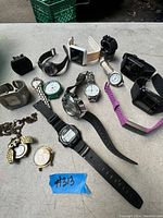 Photo showing a variety of wristwatches and pocket watches in different styles and conditions arranged on a table.