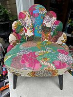 Front shot showing scalloped backrest, curved seat, and black tapered legs. Multi-colored patchwork upholstery with floral and abstract patterns visible.