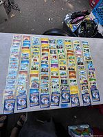 Overhead image showing about 90 Pokémon cards spread out in an organized manner on a table with backs and fronts visible.