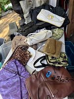 Photo showing assortment of purses on a table including brown leather bag, purple fabric bag, leopard print pouch, white clutch, gold mesh wallet, camouflage purse