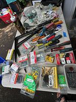 Overview of varied sizes of screws and nails in plastic packages with some hand tools alongside on a white table.
