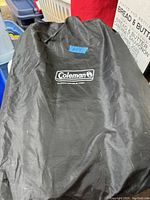 Black Coleman carrying bag with Coleman logo and 'Queen-Double High' text containing the mattress and pump.