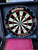 Winmau Diamond dart board mounted inside a black wooden cabinet with open door showing scoreboard.