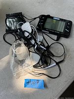 Dr. Ho's Pain Therapy System device with black control unit, attached cables, adhesive electrode pads, sponge electrode, and small black pouch on gray surface.