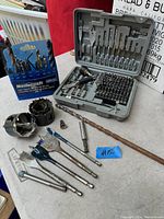 Overview of all drill bits and accessories arranged on table including hole saws, spade bits, and Mastercraft drill bit set in package.