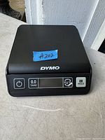 Front view of a Dymo digital scale showing the control panel with buttons and a digital display screen on a black plastic housing.