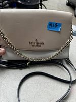 Photo of Kate Spade purse showing beige and white leather with gold logo and chain strap, also black leather adjustable strap on surface.