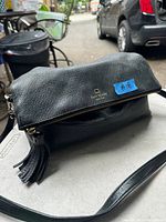 Black leather Kate Spade purse with gold logo, zipper with tassel, and long strap.