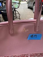 Close-up photo of the pink Kate Spade purse showing the gold logo and zipper with a blue tape tag #19.
